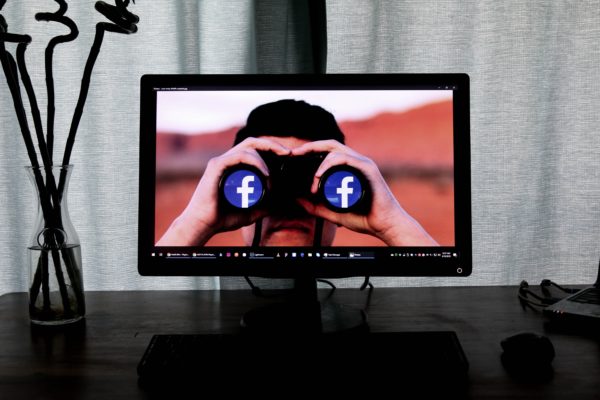 Man looking through binoculars that show Facebooks icon